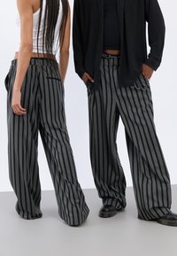 Pantaloni largi cu dungi în culori negre și gri, realizati dintr-un material confortabil, având o croială lejeră, buzunare laterale și un model texturat subtil.