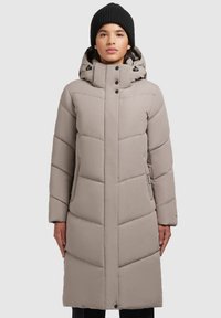 Padded long coat in a light beige color with a high collar, detachable hood, and black snap buttons. Features chevron quilted design.