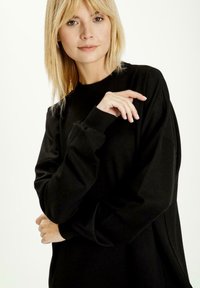 Czarna bluza z długimi rękawami i ściągaczami. Miękka tekstura, luźny krój i dekolt w serek. Minimalistyczny styl bez widocznych wzorów.