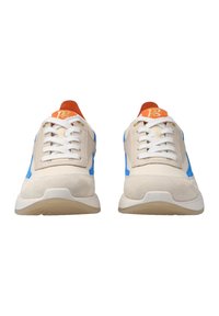 Ett par beige och blå sneakers med vita snören och orangea tunga flikar sedd framifrån på en vit bakgrund.