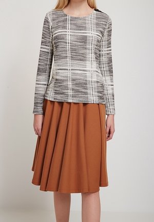 Frau trägt ein langärmeliges, grau-weiß kariertes Oberteil kombiniert mit einem hoch taillierten, knielangen, rostbraunen Faltenrock.