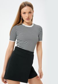 Sort og hvid kortærmet top med et zigzag-mønster, parret med højtaljede sorte short med en sidelomme og en glat tekstur.