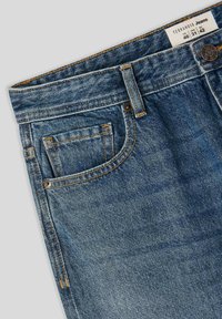 Jeans in denim di un blu medio con cuciture arancioni a contrasto, dotati di tasca anteriore e chiusura con bottone in metallo. Etichetta visibile.