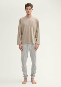 Lichtbeige lang-sleeve shirt met een ronde hals, gecombineerd met grijzige pyjamabroek. Beide kledingstukken zijn gemaakt van zachte, lichtgewicht stof.