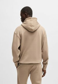 Beige hoodie with a large, adjustable hood, relaxed fit, and ribbed cuffs. Made from soft, textured fabric, paired with matching pants.