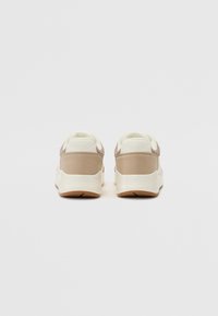 Adidași cu un upper neted de crem cu accente din suede bej, guler căptușit și o talpă din cauciuc texturată cu elemente de contrast bej.