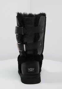 Bottine en cuir noir avec doublure en fourrure noire douce, dotée de deux brides avec ferrures métalliques. Semelle plate avec logo à l'arrière.