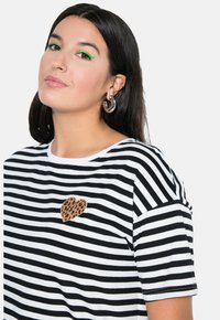 Camiseta de rayas en blanco y negro con un parche de corazón con estampado de leopardo texturizado en el lado izquierdo del pecho. Manga corta y cuello redondeado.