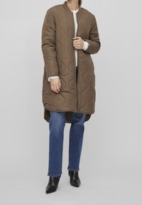 Kvadert quiltad brun jacka med ståkrage, dragkedjestängning och sidofickor. Kombinerad med blå jeans och svarta stövlar med spetsig tå.