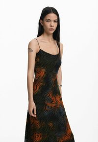 Abito a strisce nere e arancioni con silhouette aderente, spalline sottili e tessuto testurizzato che cattura la luce.