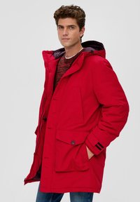 Parka rossa imbottita con cappuccio, dotata di chiusure a bottoni e zip, grandi tasche frontali e accenti a righe nere sulle maniche.