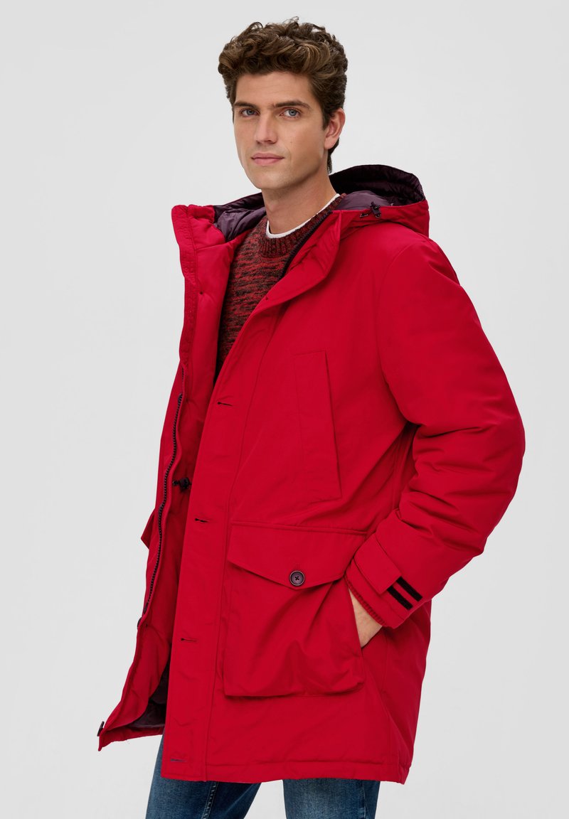 Parka rossa imbottita con cappuccio, dotata di chiusure a bottoni e zip, grandi tasche frontali e accenti a righe nere sulle maniche.