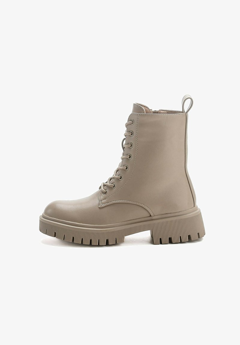 Botas de tobillo beige con cordones, con un acabado suave, puntera redonda y suela texturizada y gruesa. Incluyen un tirador trasero para facilitar su uso.