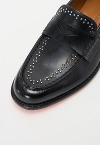 Čierne kožené loafers s hladkým povrchom, metalické štvorky pozdĺž priehlavku a dekoratívny pásik. Elegantný tvar s detailným prešívaním.
