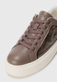 Sneaker in pelle marrone con lacci viola, suola in gomma bianca e ricami floreali su un lato. Presenta una punta arrotondata e dettagli di cucitura.
