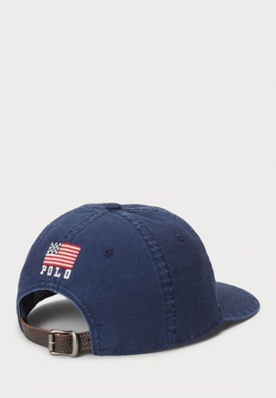 Mörkblå keps i bomull, med en broderad amerikansk flagga och 'POLO'-logotyp på baksidan. Justerbar brun rem med metallspänne.