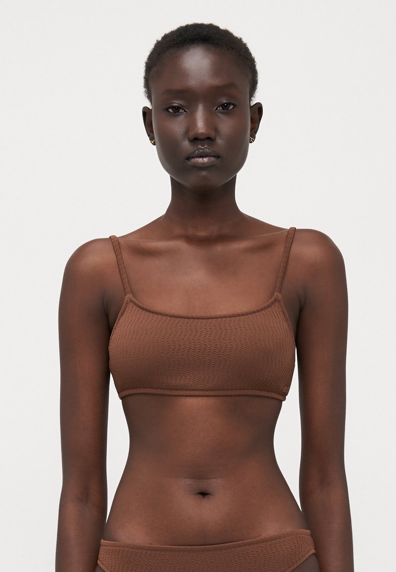 Brown textured bralette with thin straps and a square neckline, featuring a smooth, stretchy fabric and a seamless design.