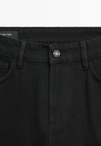 Czarne dżinsy z denimu z przodu, zapinane na guzik, z szlufkami na pasek oraz widoczną metką marki wewnątrz pasa po lewej stronie.