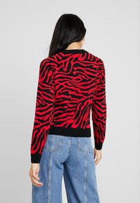 Svetr s pruhy v červené a černé barvě v tygřím vzoru, pletená tkanina, kulatý výstřih, s černým žebrovaným lemem a manžetami. Doplňeno s lehce modrými džínami.