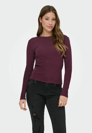 Langärmliges burgunderrotes Oberteil aus glattem Stoff mit Rundhalsausschnitt, kombiniert mit schwarzen, verwaschenen Jeans. Einfaches Design ohne Muster.