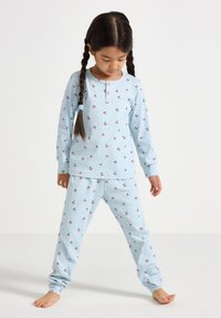 Ensemble de pyjama bleu clair composé d'un haut à manches longues et d'un pantalon, présentant une texture légèrement côtelée et de petits motifs de cerises. Détail en boutons en bois au niveau du col.
