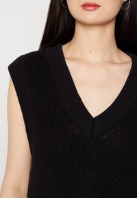Svart utanärmad stickad tröja med djup V-ringning, ribbad textur och subtila öppenstickade detaljer vid halsringningen.
