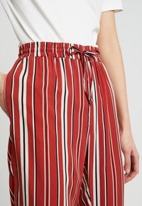 Pantalon à jambes larges rayé rouge et blanc avec taille élastique et cordon de serrage. Confectionné dans un tissu doux avec une texture légère.