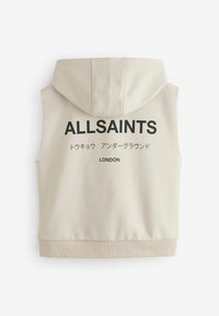 Beež kapuutsita vest, mille seljal on suur must "ALLSAINTS" tekst, lisaks jaapanikeelne tekst ja all "LONDON".