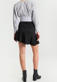 Gestreifte Langarmbluse mit gerafftem Rücken, kombiniert mit einem schwarzen ausgestellten Rock. Das Outfit wird durch Knöchelstiefel abgerundet.