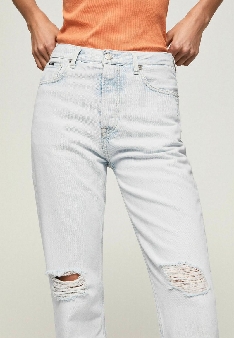 Hellblaue Jeans im lässigen Schnitt, mit aufgerissenen Kniebereichen und subtilen Ausbleichungen. Klassisches Fünf-Taschen-Design mit Knopfverschluss.