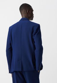 Blazer blu navy in tessuto strutturato, slim fit, con rever a punta e spacco singolo sul retro, dotato di polsini a quattro bottoni.