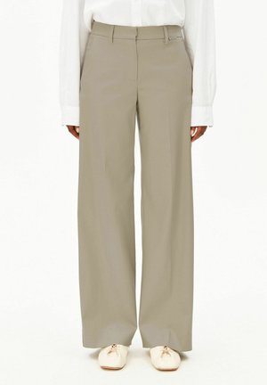 Beige Hosen mit weitem Bein, getragen mit einem weißen Langarmhemd und hellbeigen flachen Schnürschuhen, von der Taille bis zu den Füßen gezeigt.