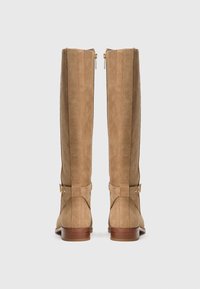 Pair of tan suede knee-high boots with low wooden heels and gold side zipper and buckle details, viewed from the back.