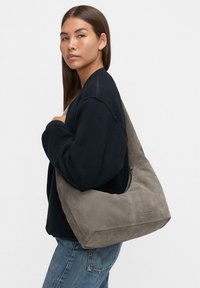 Zamszowa torba hobo w stonowanym szarym kolorze. Miękka tekstura, duży kształt i zamknięcie na zamek błyskawiczny. Subtelny detal z logo po jednej stronie.