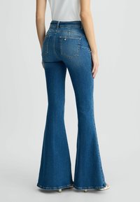 Jeans in denim blu a zampa di elefante con vita alta, dotati di due tasche posteriori e una texture sbiadita, mostrati da dietro.