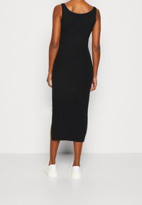 Czarna prążkowana sukienka midi z okrągłym dekoltem, bocznymi rozcięciami i dopasowanym krojem, zestawiona z białymi trampkami dla casualowego wyglądu.
