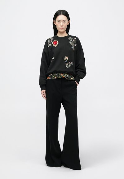 Mustmustree, mille lillede ja südame brodeeringuga, koos lahtiste mustade pükste paariga. Tekstuuriga materjalid värviliste mustritega äärmisel äärel.