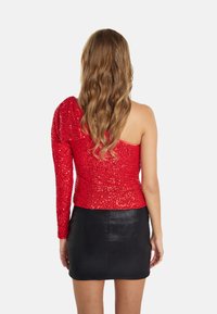Top rosso con paillettes dal design asimmetrico; una manica lunga e una spalla scoperta, abbinato a una minigonna nera. Tessuto liscio.
