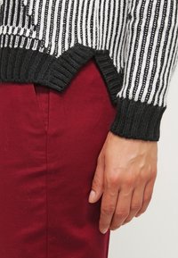 Svartvitt randig stickad tröja med ribbade ärmslut, med rundad nederkant. Kombinerad med bordeauxfärgade byxor.