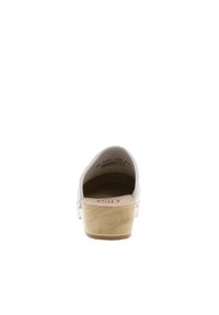 White wooden clogs with a solid wood sole, perforated design on the upper, padded interior, featuring a circular red logo on the heel.