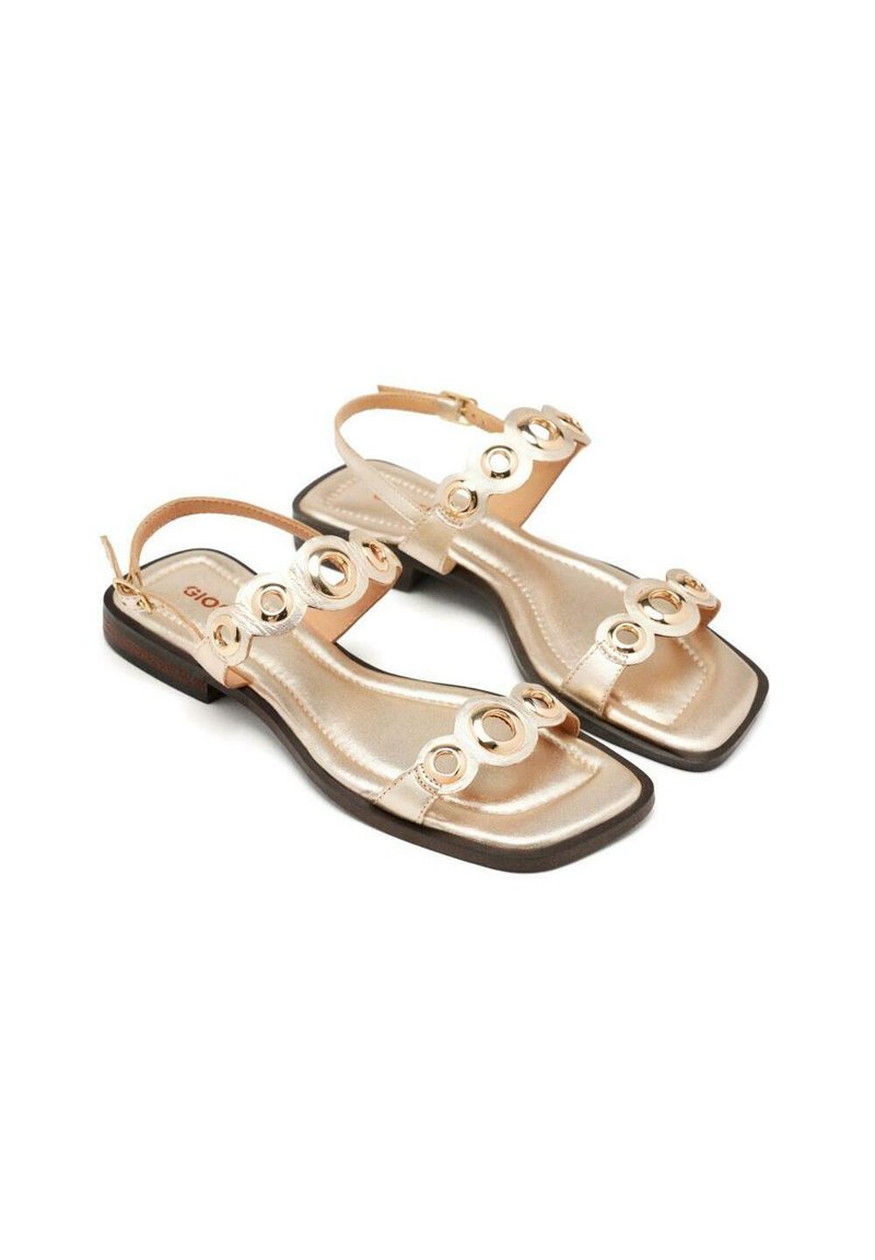 Sandali metallici dorati con suola piatta, caratterizzati da applicazioni a forma rotonda sulle cinghie e una cinghia alla caviglia per una vestibilità sicura. Design con punta quadrata.