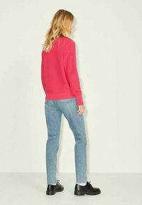 Maglione a coste rosa brillante con maniche lunghe, abbinato a jeans dritti azzurri e scarpe nere, visto da dietro.
