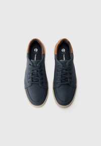 Tênis de lona azul-marinho com detalhes em couro castanho no calcanhar, bico arredondado e design de atacadores com seis ilhós. Sola de borracha cremosa.