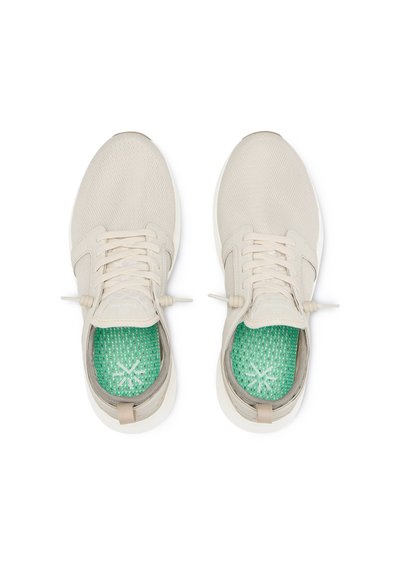 Chaussures de sport beiges avec un dessus en mesh et des lacets, dotées de semelles intérieures texturées vertes avec un emblème de logo.