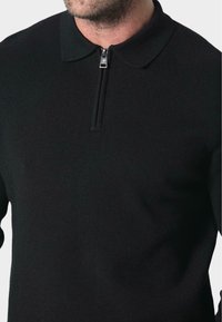 Svart strikket genser med glidelåskrage, med en jevn tekstur og en avslappet passform. Minimalistisk design, uten synlige mønstre eller detaljer.