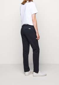 Marineblauwe tapered broek van een katoenmix, met een achterzak, een minimalistisch merketiket, een vlakke voorkant en een gladde textuur. Gecombineerd met een wit t-shirt.