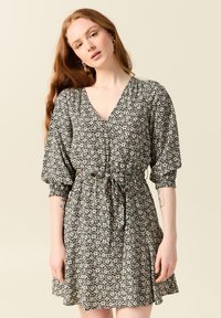 Svart blommig klänning med V-ringning, puffärmar, knytmidja och utsvängd kjol. Har ett litet vitt blommönster på en mörk bakgrund.