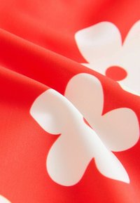 Roter Stoff mit großen, sich überlappenden weißen Blumenmustern. Die Oberfläche wirkt glatt und leicht glänzend, mit lebendigen Farben.