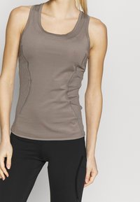 Brun idrottstopp med en figursydd design, texturerade sidopaneler och båtutskurna halsringning, kombinerat med svarta leggings.