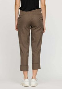 Pantalons courts à carreaux marron avec un ourlet retroussé, présentant une texture de tissu lisse et deux poches arrière, associés à des baskets blanches.